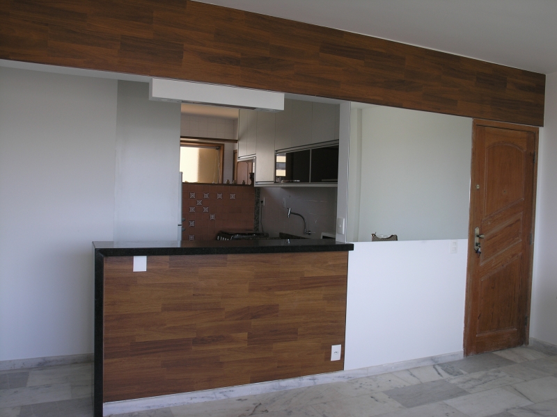 Abertura de parede integra a cozinha e a sala através de balcão em granito e madeira.