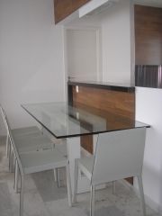 Linda mesa com tampo de vidro, cadeiras em couro branco em harmonia com balco revestido com madeira e granito preto.