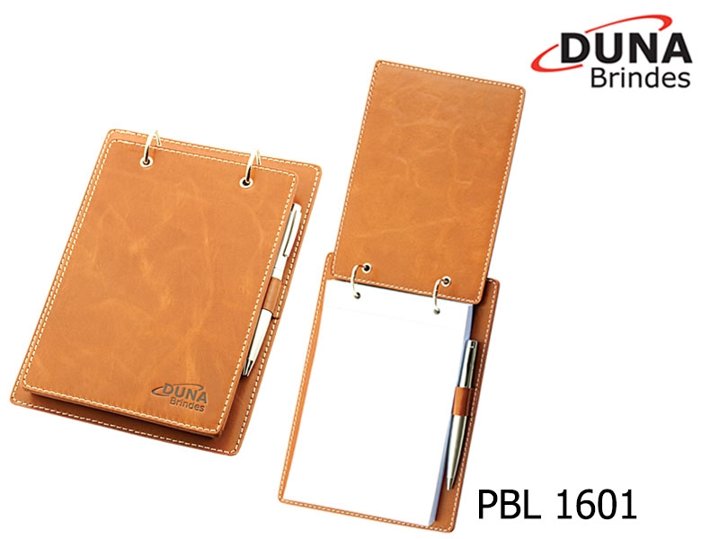 Porta Bloco PBL 1601 - Personalizado com seu logotipo em baixo relevo, contendo ferragem duas argolas, porta caneta e bloco de anotações serrilhado com 150 folhas medindo 20 x 14 cm (caneta não inclusa).